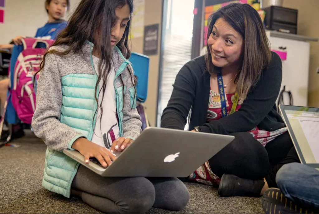 Teacher and student sitting on floor using laptop